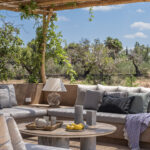 Detailansicht der durchgehenden Sitzbank mit grauen Kissen unter der Pergola aus Schilfrohr, mit rundem Holztisch