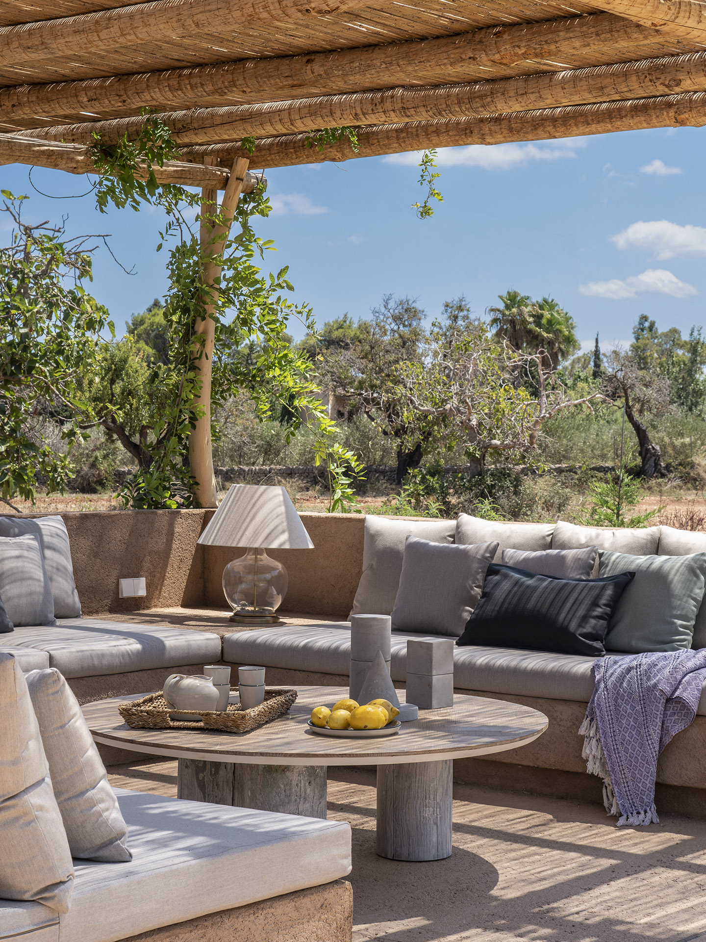 Detailansicht der durchgehenden Sitzbank mit grauen Kissen unter der Pergola aus Schilfrohr, mit rundem Holztisch