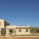 Zweigeschossiges Steinhaus mit eingeschossigem Anbau, blauem Himmel und Swimmingpool im Hintergrund