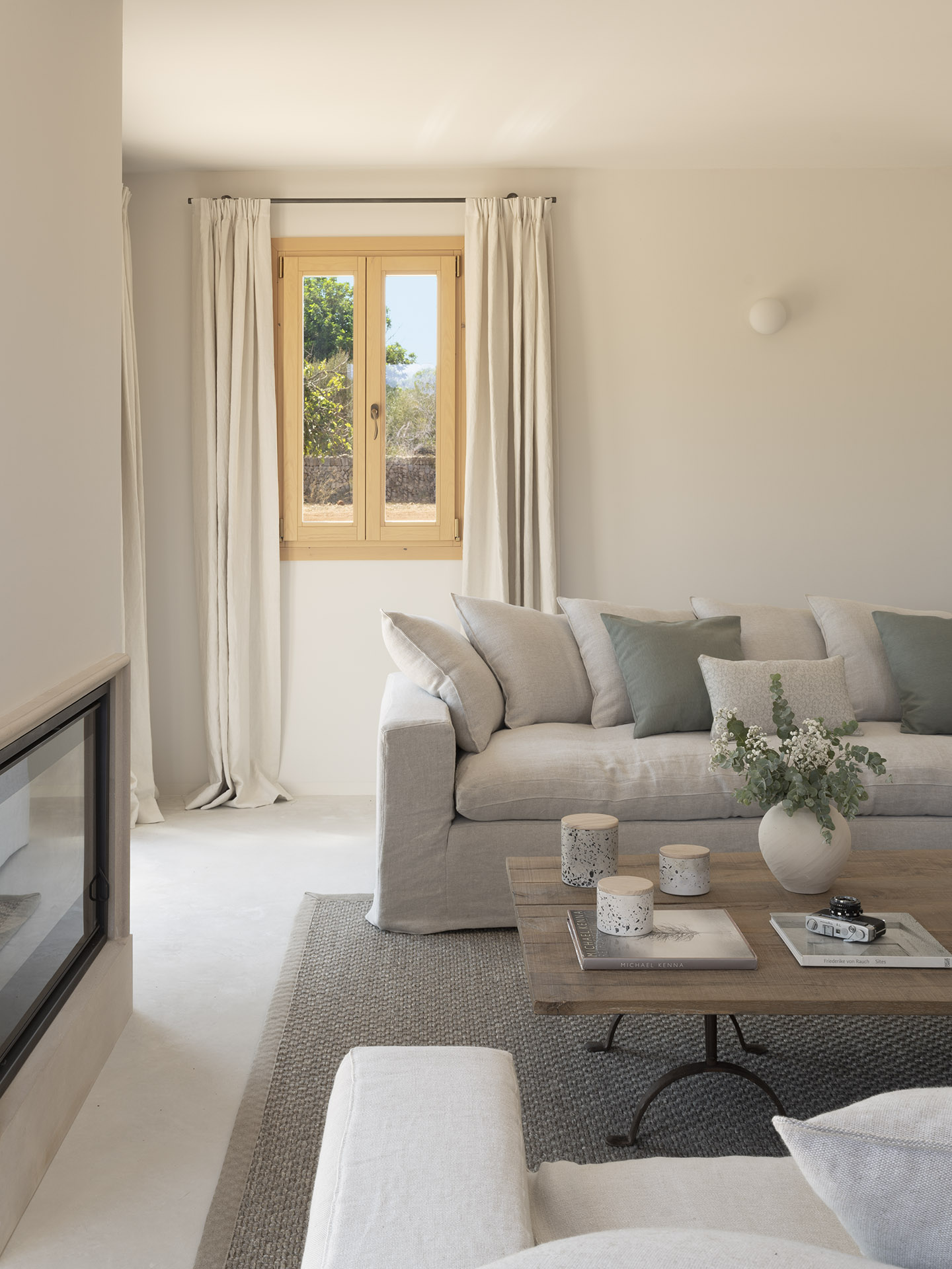 Detailansicht des Wohnzimmers mit hellem Leinensofa, grünen Kissen, Holztisch und Fenster mit Vorhängen