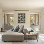 Helles Wohnzimmer mit grauem Modulsofa, blaugrünem Gemälde, langen Vorhängen und großen Holzfenstern zum Garten