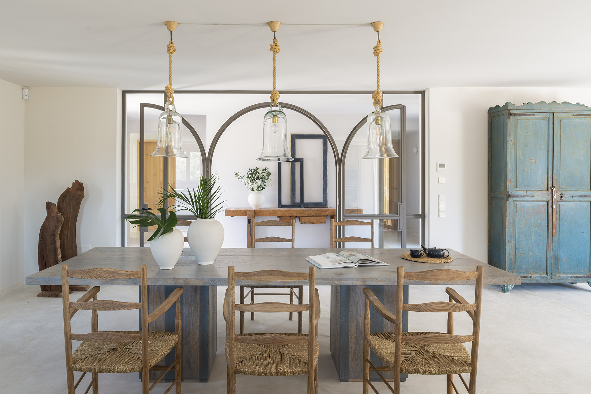 Essbereich mit grauem Tisch, Holzstühlen mit Geflechtsitz, Hängeleuchten aus Glas und blauem Schrank