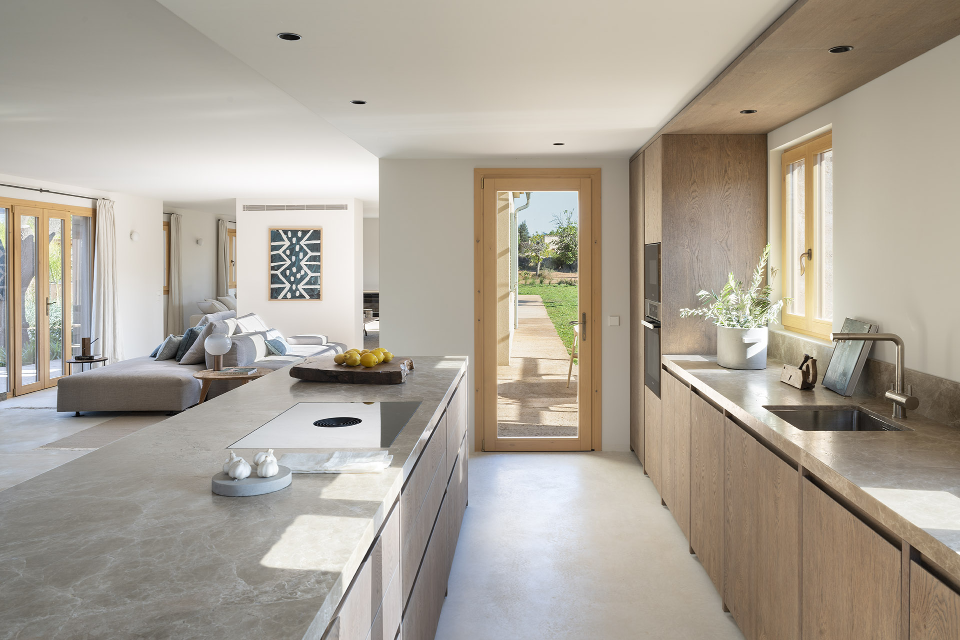 Küche mit Kochinsel und Steinarbeitsplatte, Holzschränken, Gartentür und Wohnzimmer im Hintergrund