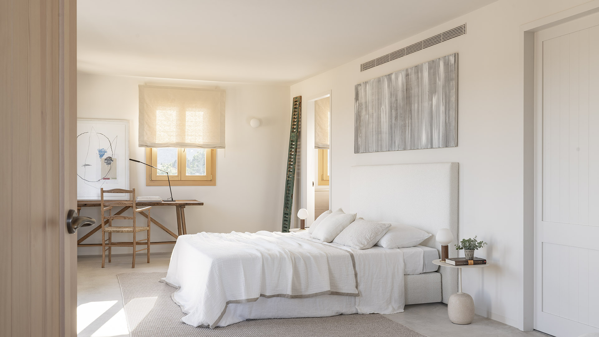 Helles Schlafzimmer mit weißem Bett, Holzschreibtisch am Fenster und hellem Rollo