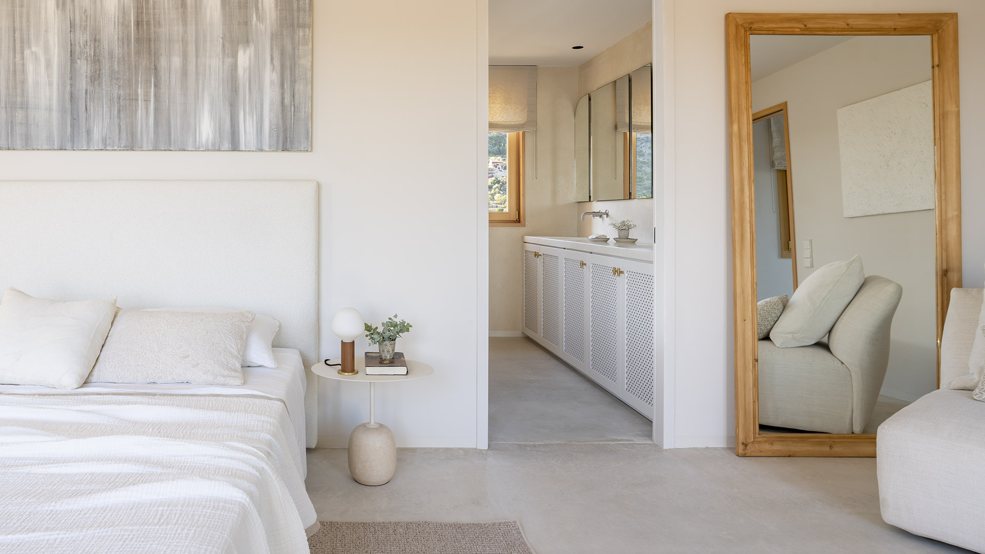 Schlafzimmer in Ecru-Tönen mit weißem Kopfteil, Holzspiegel und Ensuite-Bad im Hintergrund