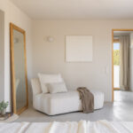Schlafzimmer mit weißer Chaiselongue, Standspiegel mit Holzrahmen und offener Tür zum Flur