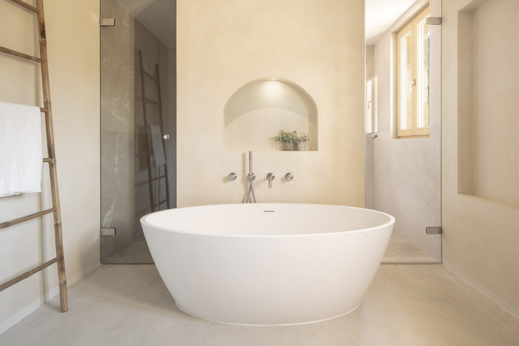 Hauptbadezimmer mit freistehender weißer Badewanne, Rundbogennische, Steindusche und poliertem Betonboden