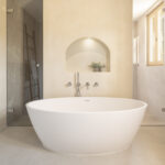 Hauptbadezimmer mit freistehender weißer Badewanne, Rundbogennische, Steindusche und poliertem Betonboden