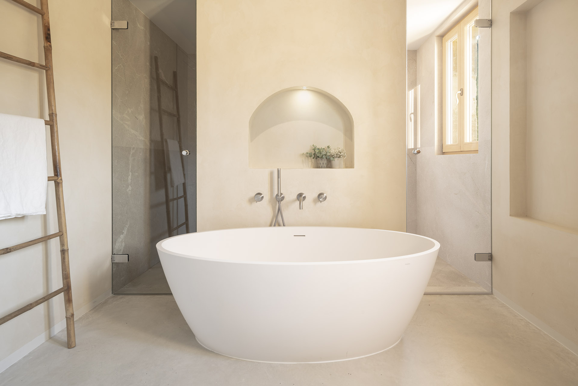 Hauptbadezimmer mit freistehender weißer Badewanne, Rundbogennische, Steindusche und poliertem Betonboden
