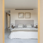 Schlafzimmer zwischen offenen mallorquinischen Fensterläden, mit grauem Kopfteil, zwei Bildern und poliertem Betonboden
