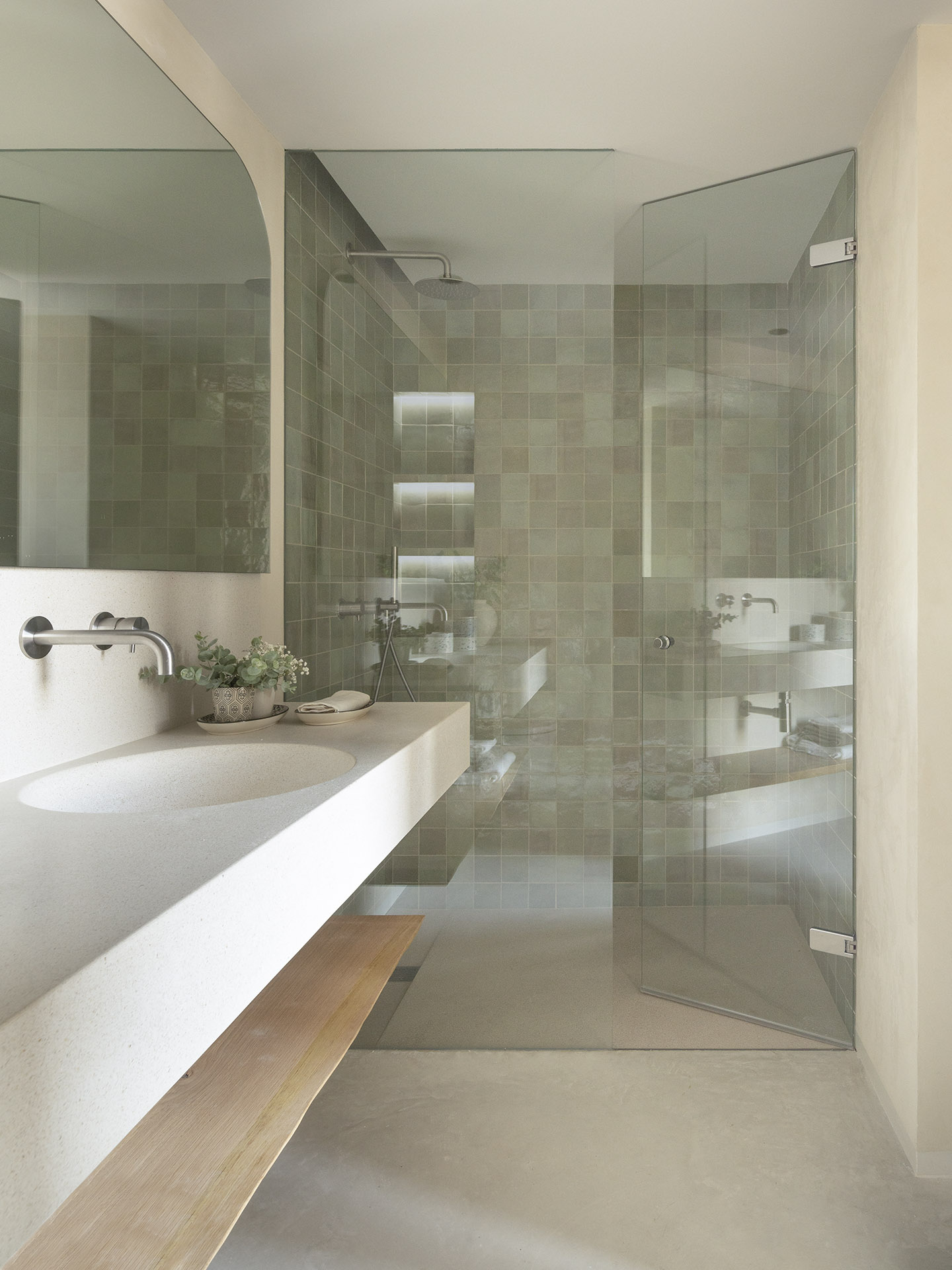 Badezimmer mit Dusche aus grünen Zellige-Fliesen, Terrazzo-Waschtisch, Holzablage und Duschwand aus Glas