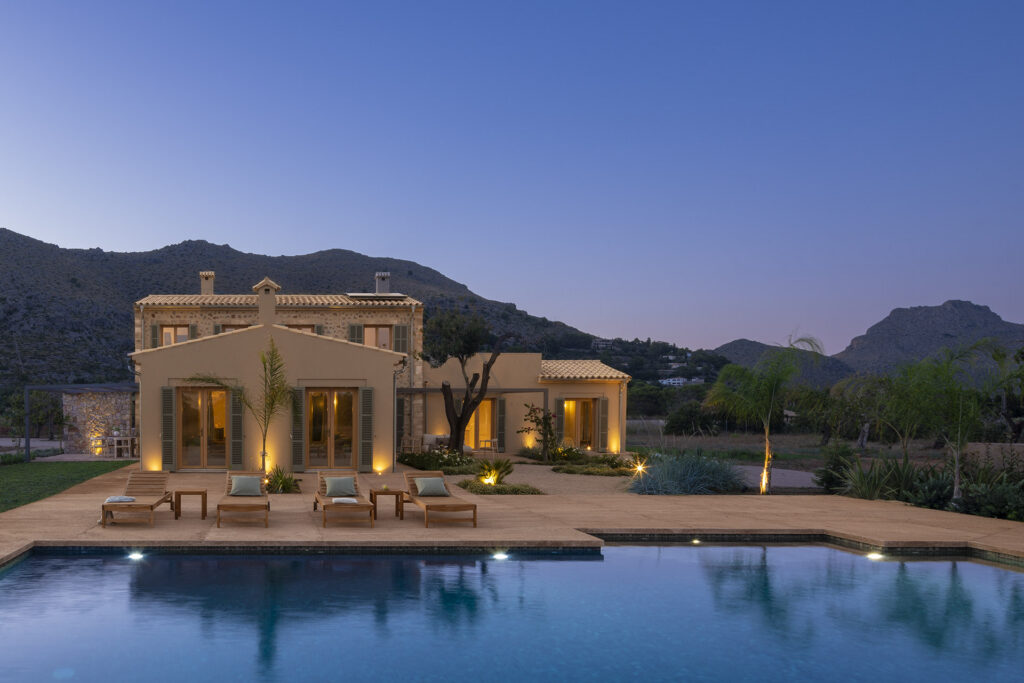 Beleuchtete Fassade aus Stein mit mallorquinischen Fensterläden, vom Swimmingpool aus gesehen, mit Spiegelungen im Wasser