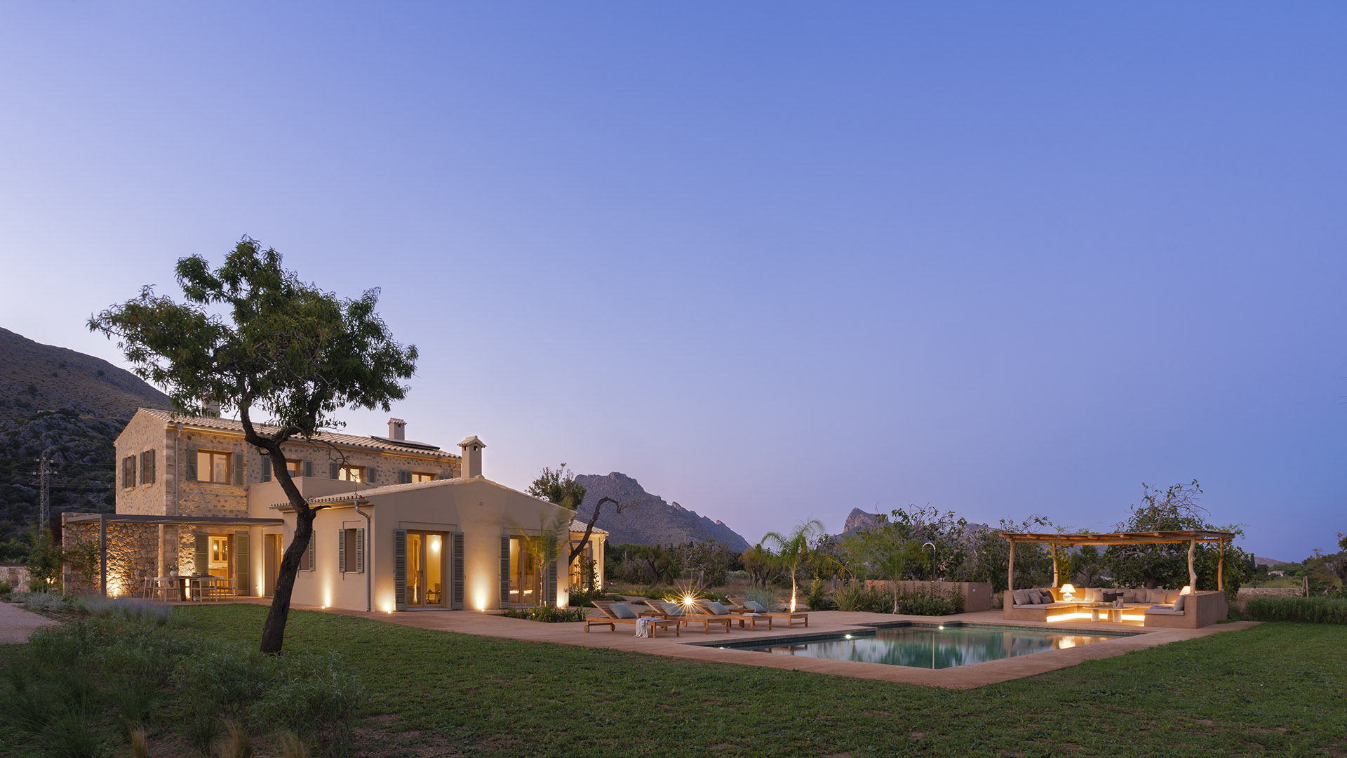 Panoramablick am Abend mit einem Baum im Vordergrund, dem Haus, dem Pool und der Chill-out-Zone