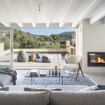Living room of SJ61 with lit fireplace, white beams and a terrace with pool beyond