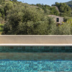 Detail of the swimming pool with green lining, turquoise water and Mediterranean vegetation in the background