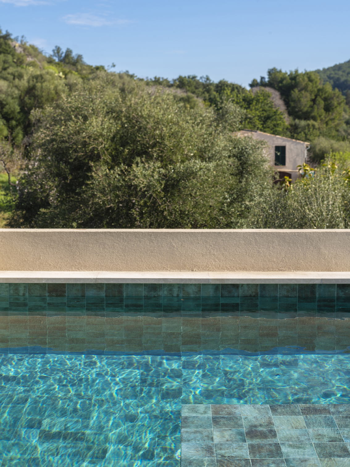 Detail of the swimming pool with green lining, turquoise water and Mediterranean vegetation in the background
