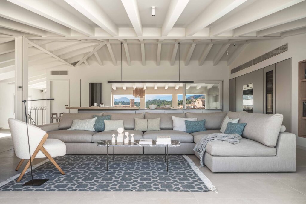 Grey modular sofa with blue cushions, geometric rug and white beamed ceiling