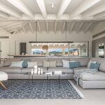 Grey modular sofa with blue cushions, geometric rug and white beamed ceiling
