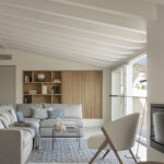 Corner of the living room with light wood shelving, grey sofa, white armchair and beamed ceiling
