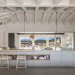 Kitchen with a large white island, light wood breakfast bar, stools and a window overlooking the village