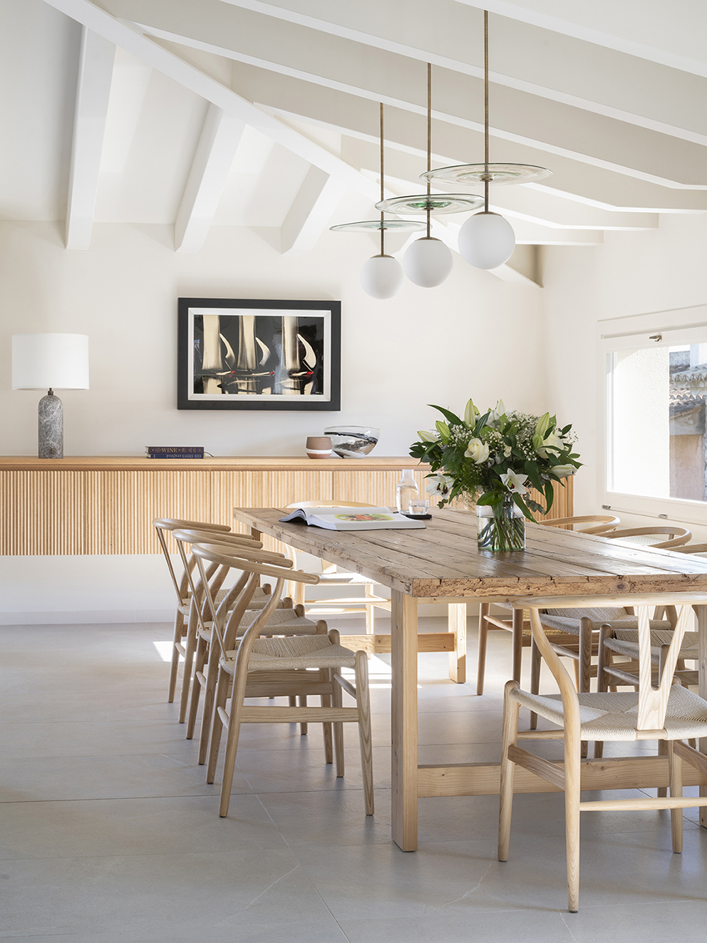 Dining room with weathered wooden table, light wood chairs and white globe lamps