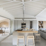 Light grey kitchen island with wooden worktop, stools and white beamed ceiling