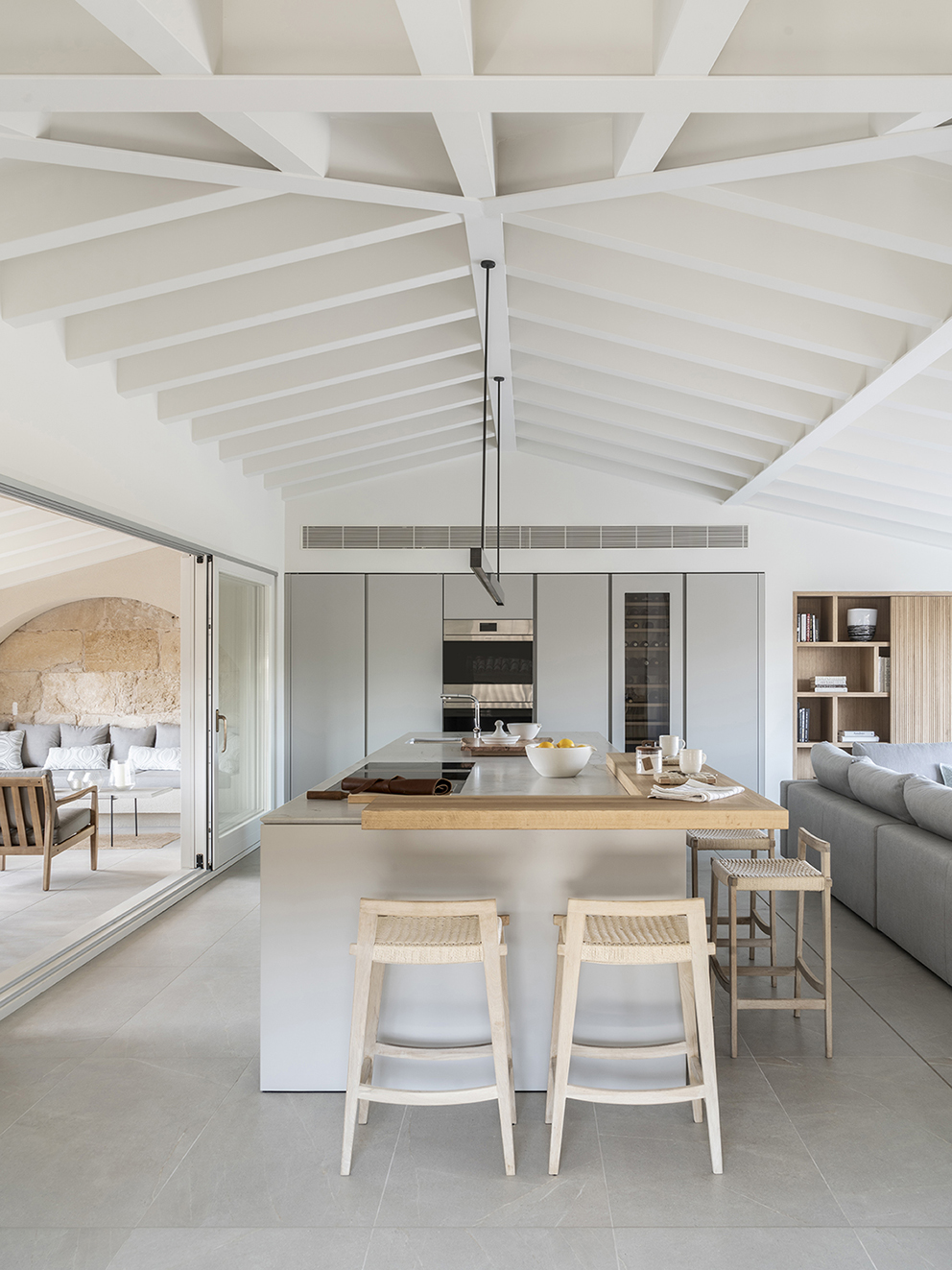 Light grey kitchen island with wooden worktop, stools and white beamed ceiling