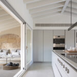 Light grey kitchen with island and tall units, opening onto the terrace with a stone arch
