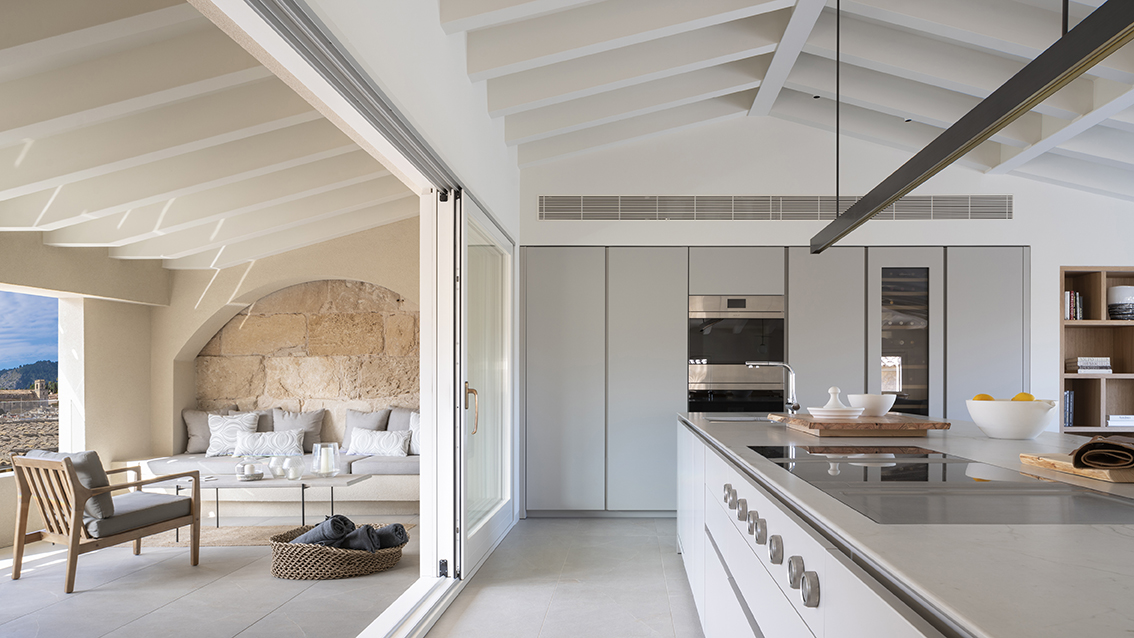 Light grey kitchen with island and tall units, opening onto the terrace with a stone arch