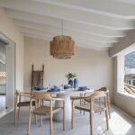 Terrace with a round white table, blue tableware, wooden chairs and a natural fibre lamp