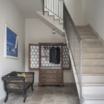 Entrance hall with light stone staircase, metal balustrade, antique wardrobe and cane bench