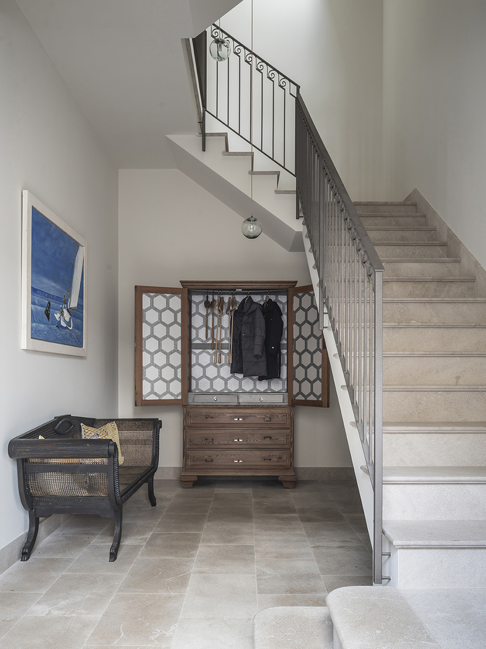 Entrance hall with light stone staircase, metal balustrade, antique wardrobe and cane bench