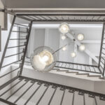 Stairwell seen from below with dark iron balustrade and glass lamps