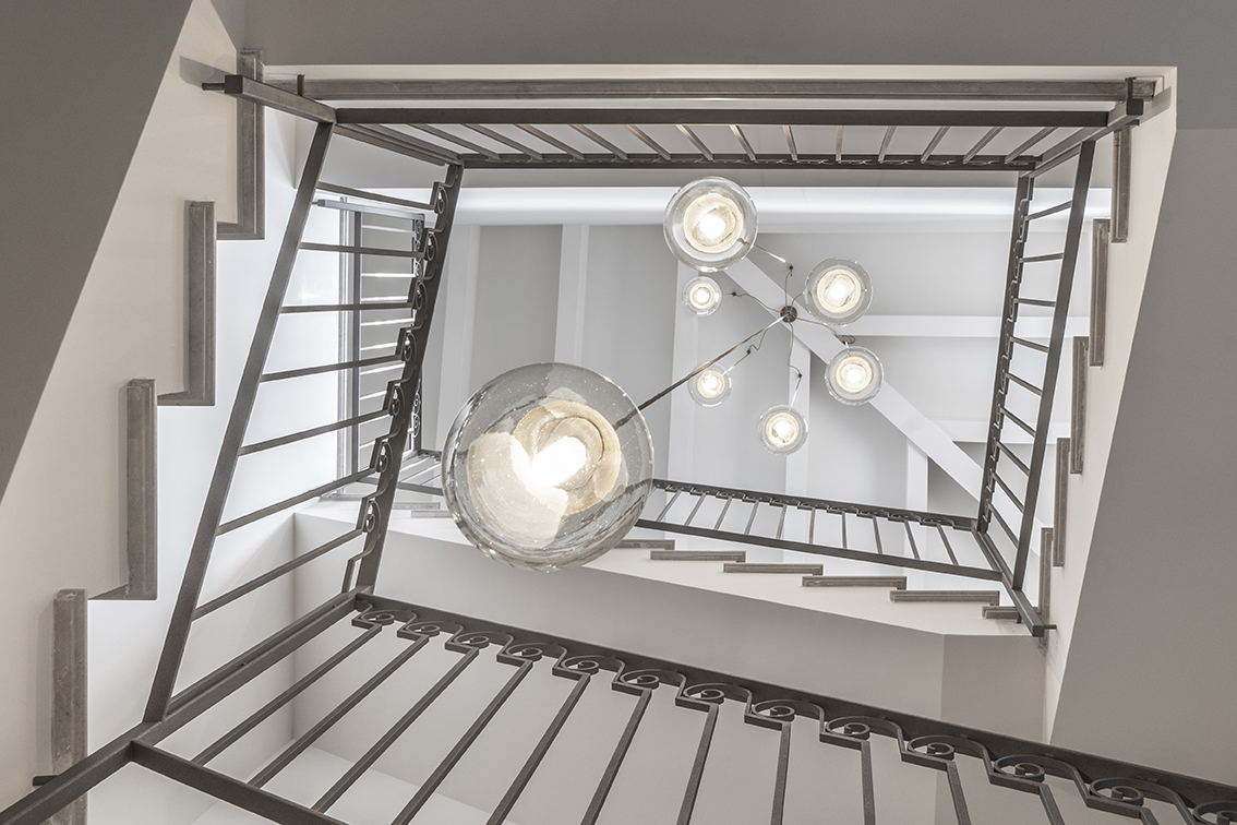 Stairwell seen from below with dark iron balustrade and glass lamps