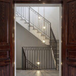 Staircase seen through dark wooden doors, with wrought iron balustrade and pendant lamps