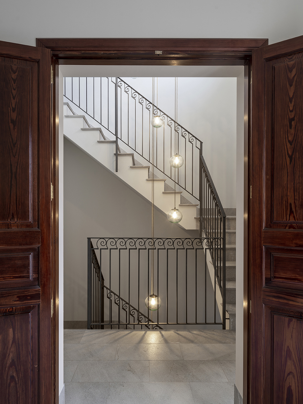 Staircase seen through dark wooden doors, with wrought iron balustrade and pendant lamps