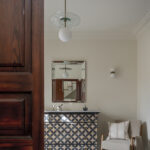Chest of drawers with geometric motifs, bevelled-frame mirror, beige armchair and white globe lamp