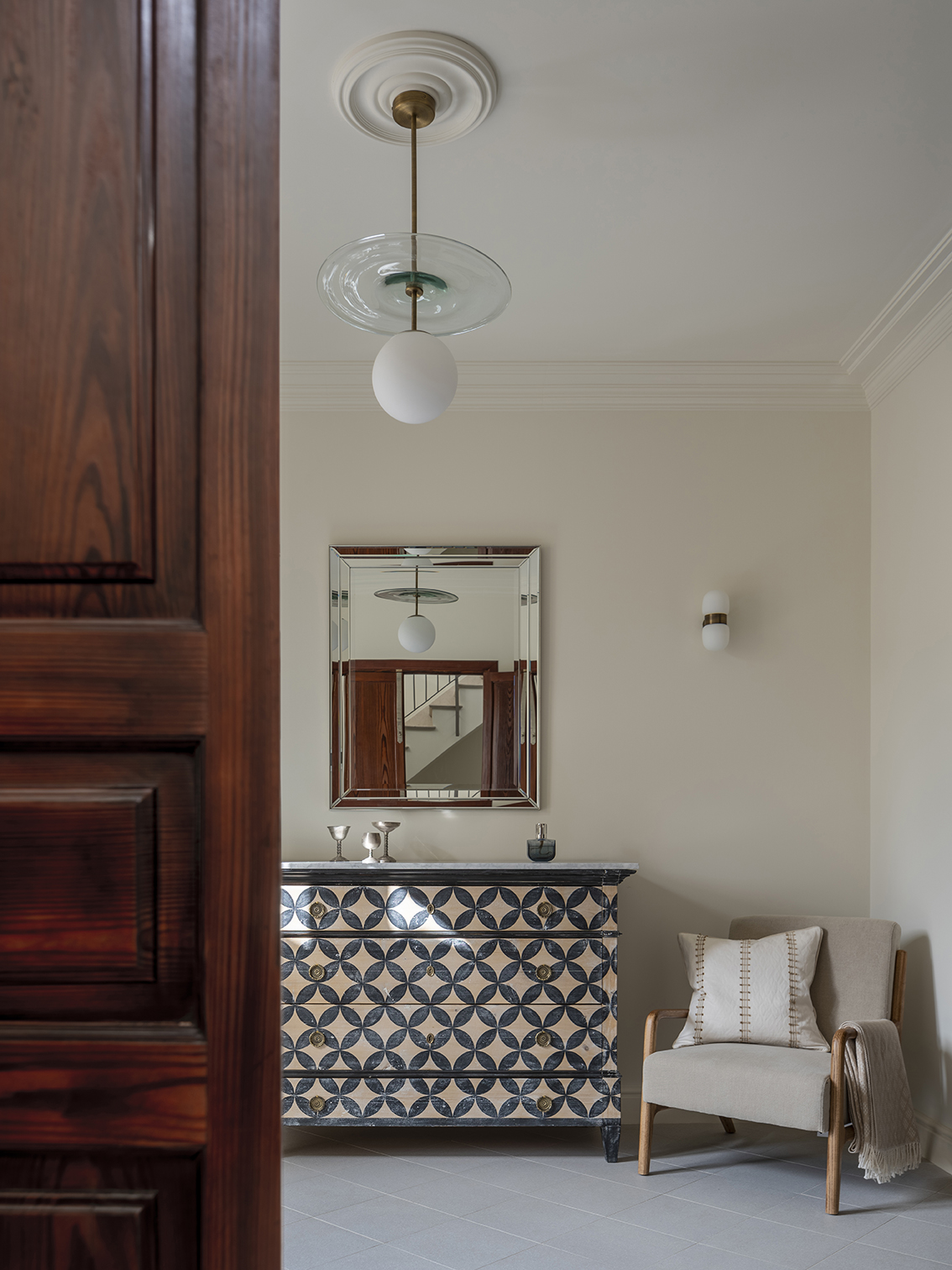 Chest of drawers with geometric motifs, bevelled-frame mirror, beige armchair and white globe lamp