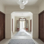 Wide hallway with moulded arch, dark wooden doors, blue-grey rugs and natural light at the far end