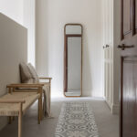 Corner with a wooden bench and rope, tall mirror and rug with an encaustic tile pattern