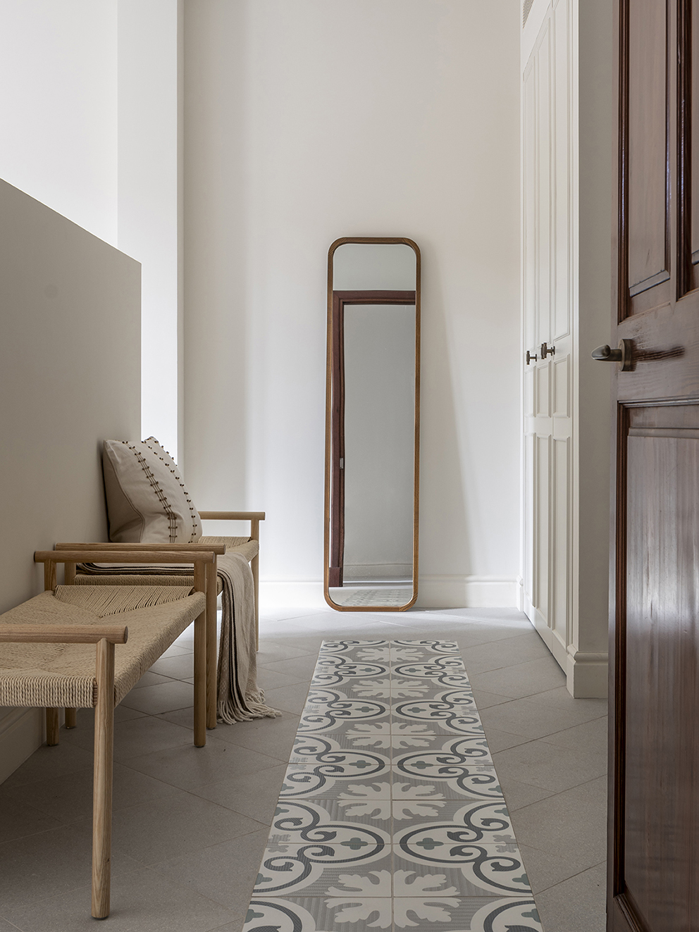 Corner with a wooden bench and rope, tall mirror and rug with an encaustic tile pattern