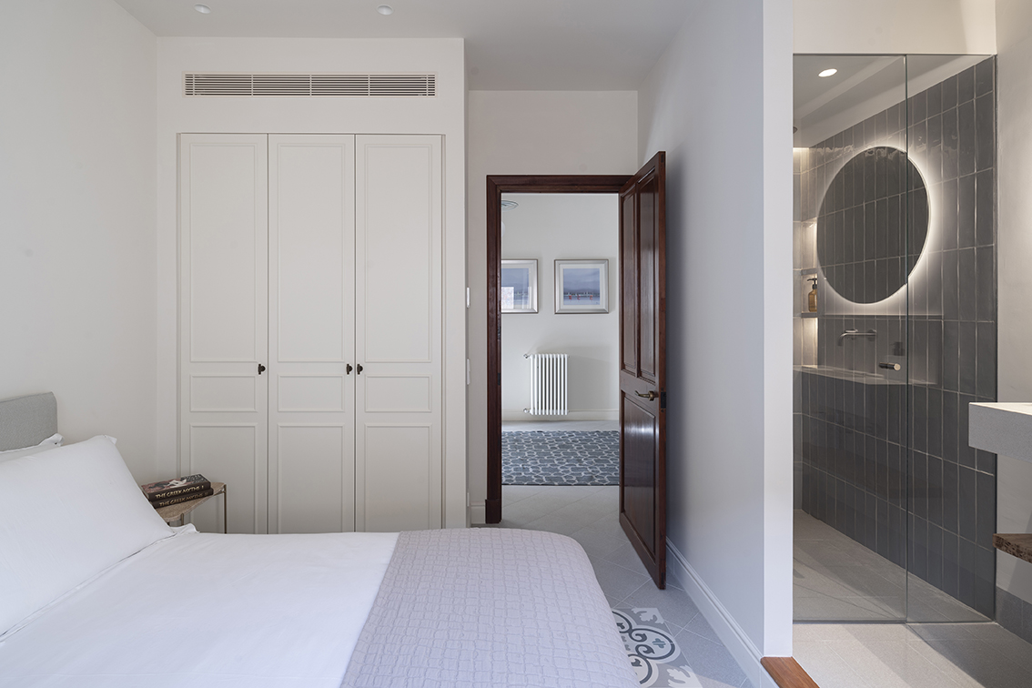 Bedroom with open door to the hallway, white wardrobe with mouldings and en suite shower with round mirror