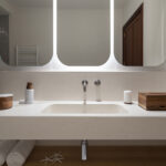Washbasin built into a light worktop with three rounded backlit mirrors and a wooden shelf