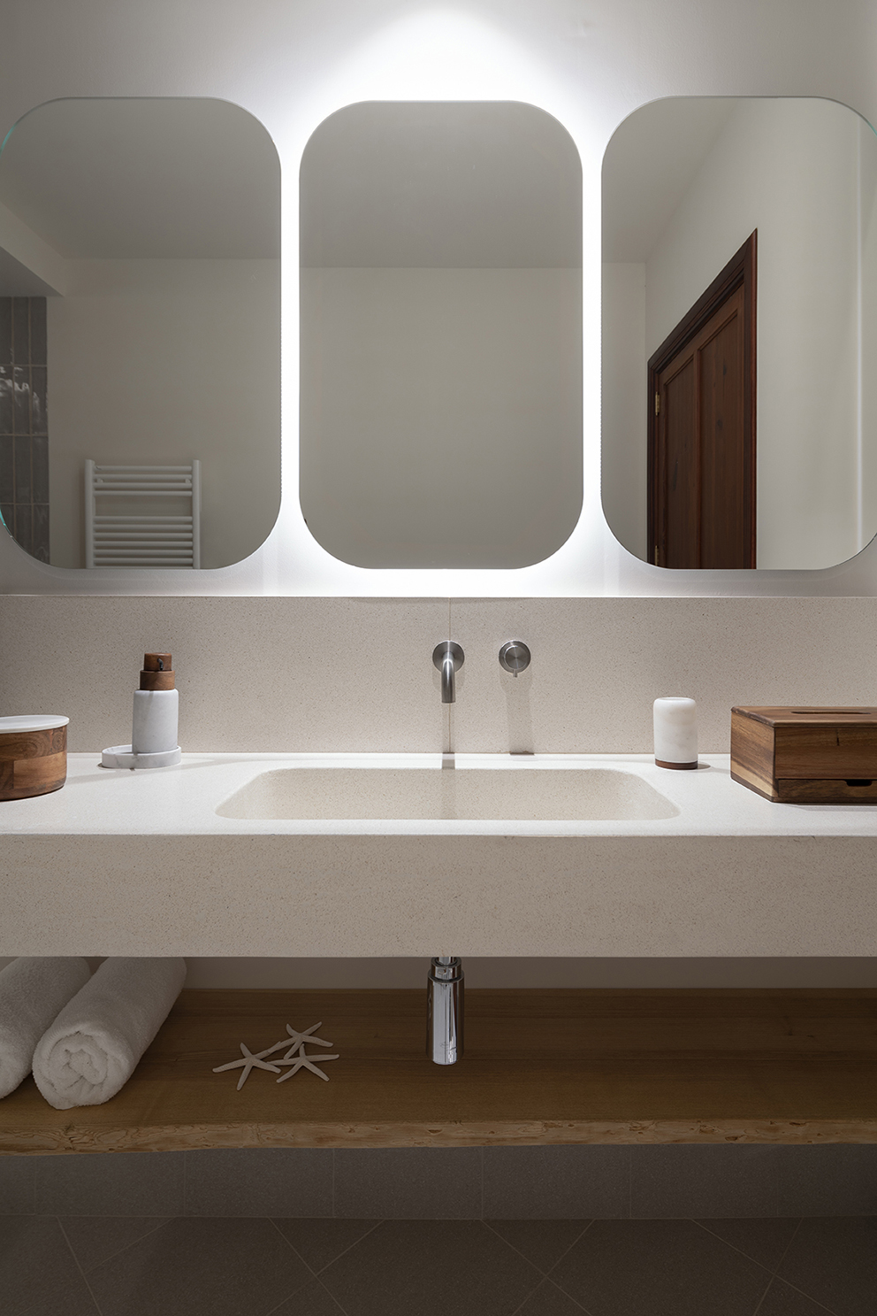 Washbasin built into a light worktop with three rounded backlit mirrors and a wooden shelf
