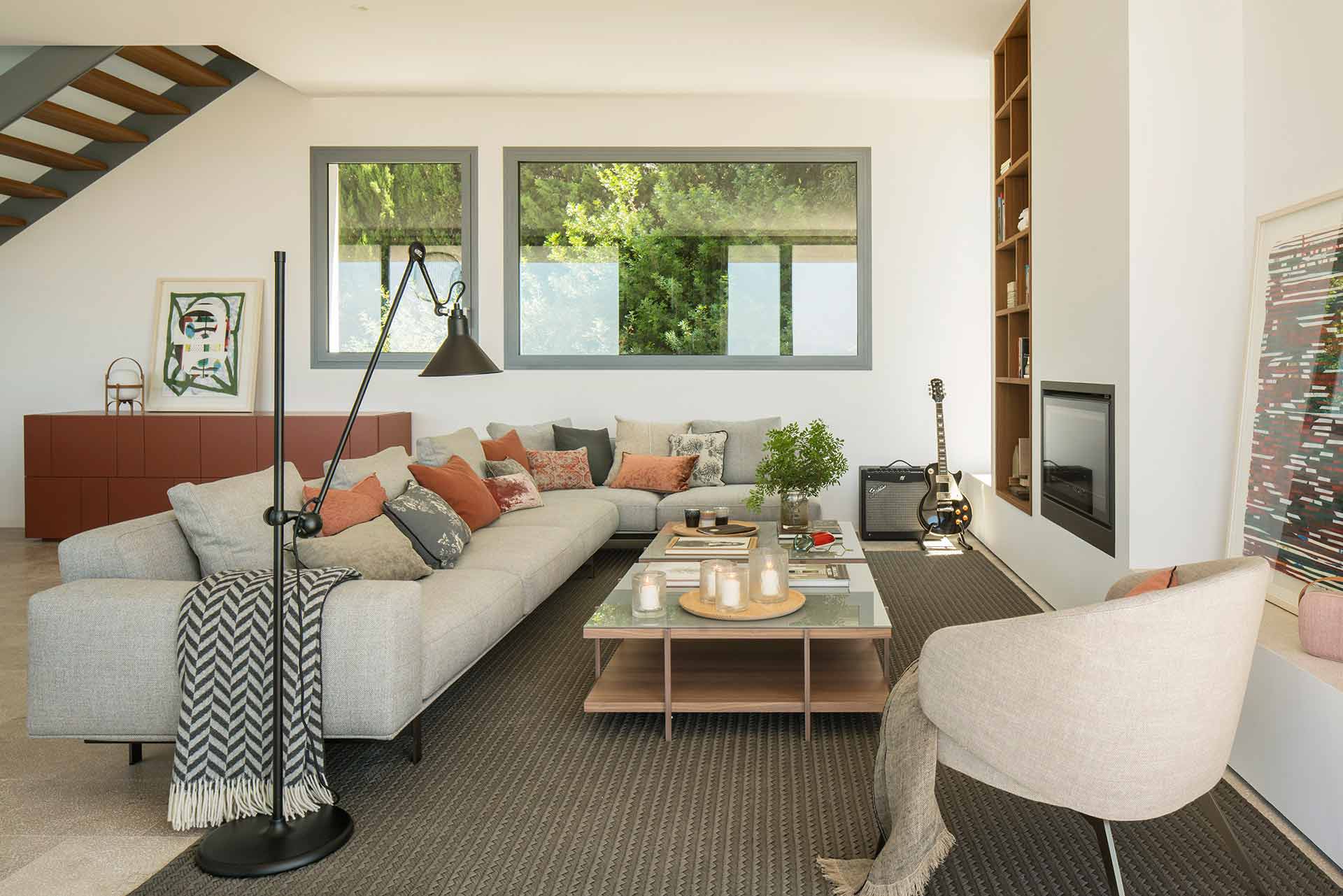 Bright living room with grey corner sofa, terracotta cushions, reddish sideboard, fireplace and grey windows