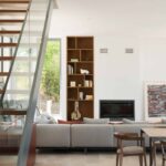 Living room with built-in timber shelving, fireplace, grey sofa and staircase with glass balustrade