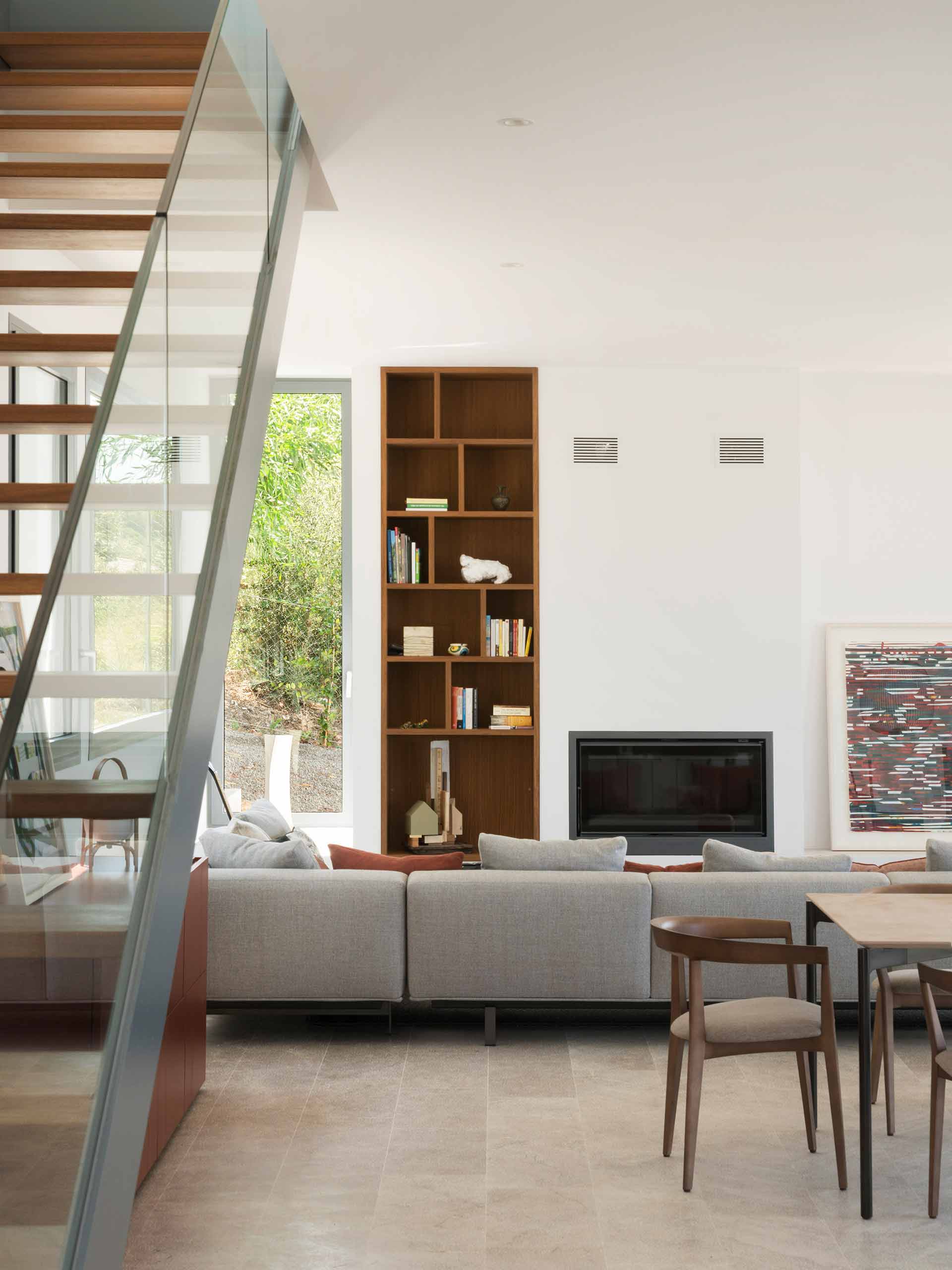 Living room with built-in timber shelving, fireplace, grey sofa and staircase with glass balustrade
