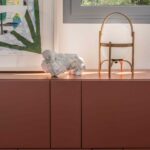 Detail of terracotta sideboard with portable wooden lamp, white sculpture and painting