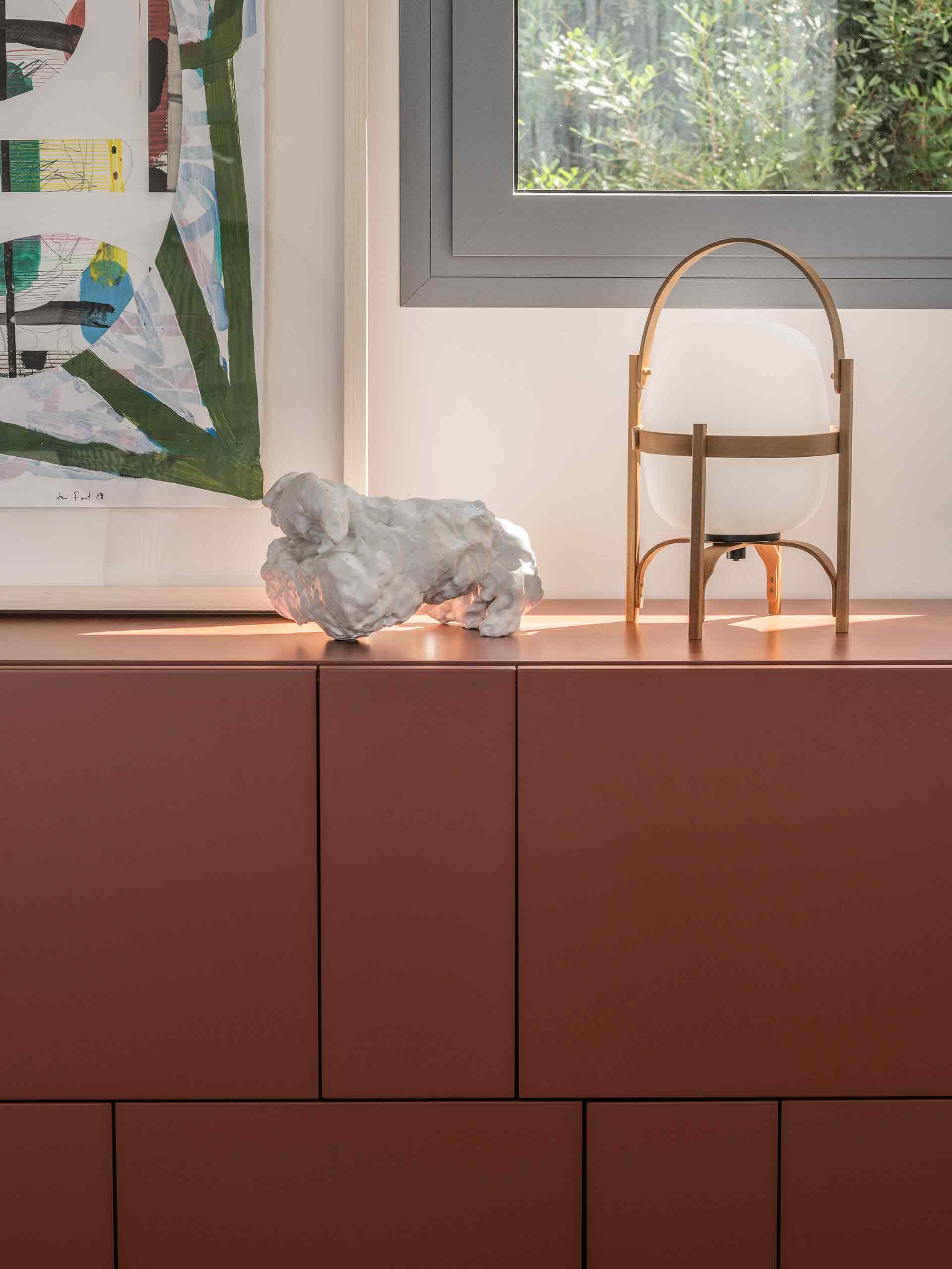 Detail of terracotta sideboard with portable wooden lamp, white sculpture and painting