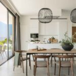 Dining area and kitchen with large sliding window open to the terrace and pale stone floor